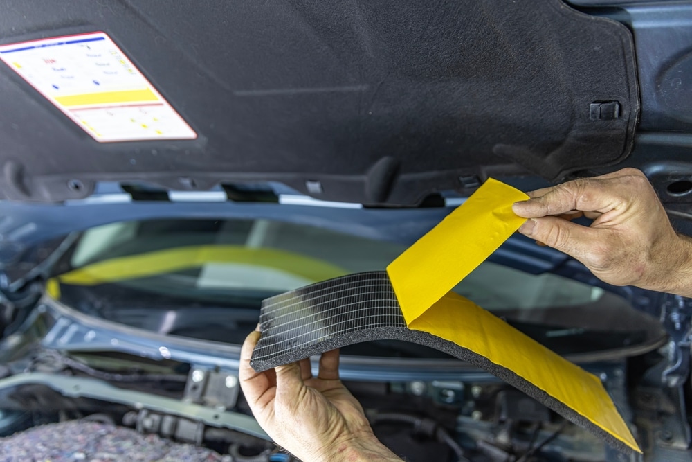Auto service worker applies soundproof sponge material to the hood of the car