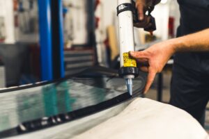 Worker applying an adhesive sealant to car windscreen preparing for replacement.